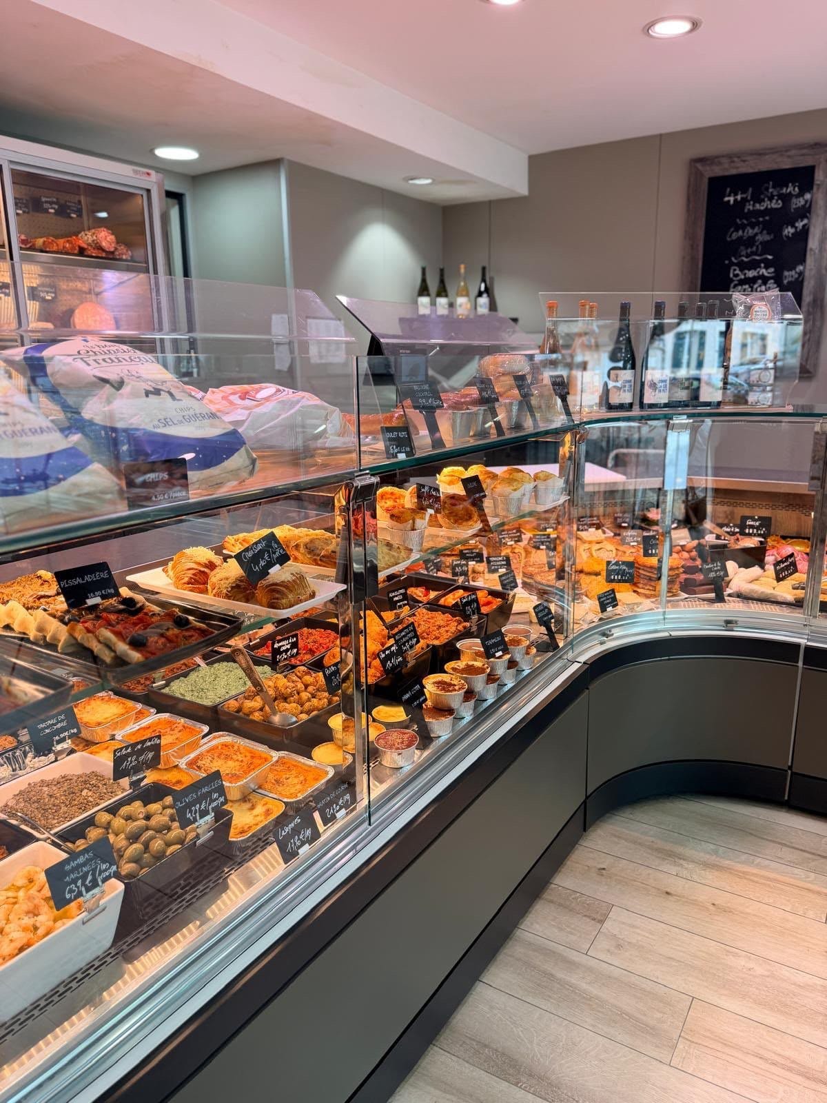 L'intérieur de la boutique : vitrines traiteur, charcuterie et boucherie, vins et produits d'épicerie