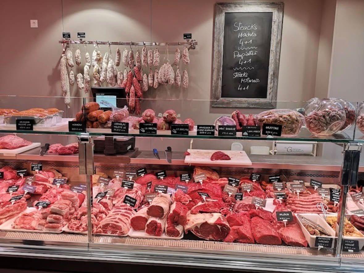 Le comptoir de la boucherie : pièces de bœuf, veau, porc et volailles en vitrine réfrigérée, saucissons suspendus en arrière-plan