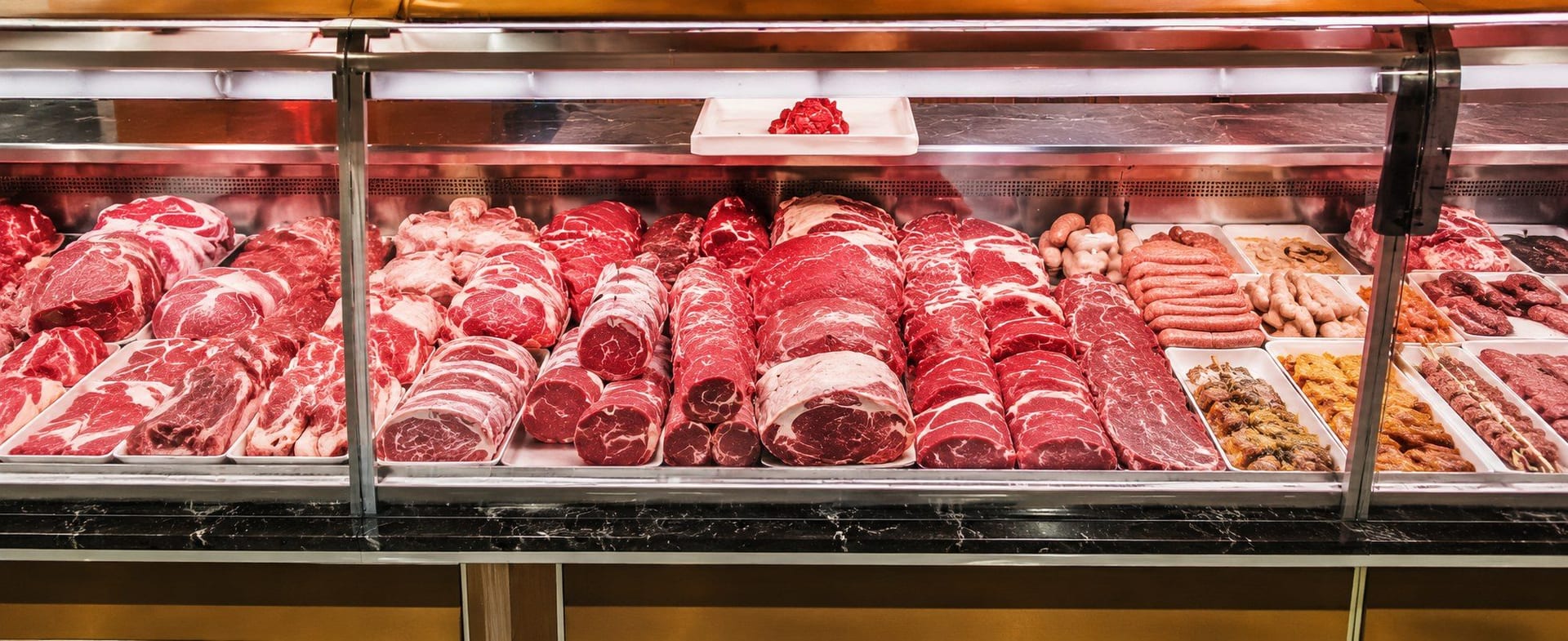 Vitrine réfrigérée garnie de pièces de bœuf, rôtis, saucisses et brochettes marinées